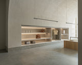 A retail space with arched ceilings and built-in shelves. The shelves display neatly arranged travel items, including classic carry-on, hybrid carry-on suitcases, metro weekender, metro duffel, kiyo uvc water bottles, sevilla top and sevilla dress, with warm, ambient lighting.