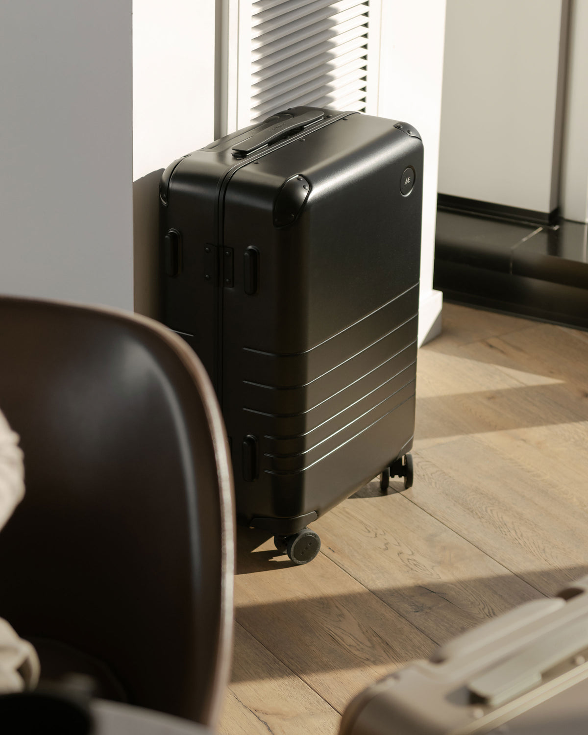 A Hybrid carry-on in obsidian positioned against a wall in a sunlit room, casting soft shadows.