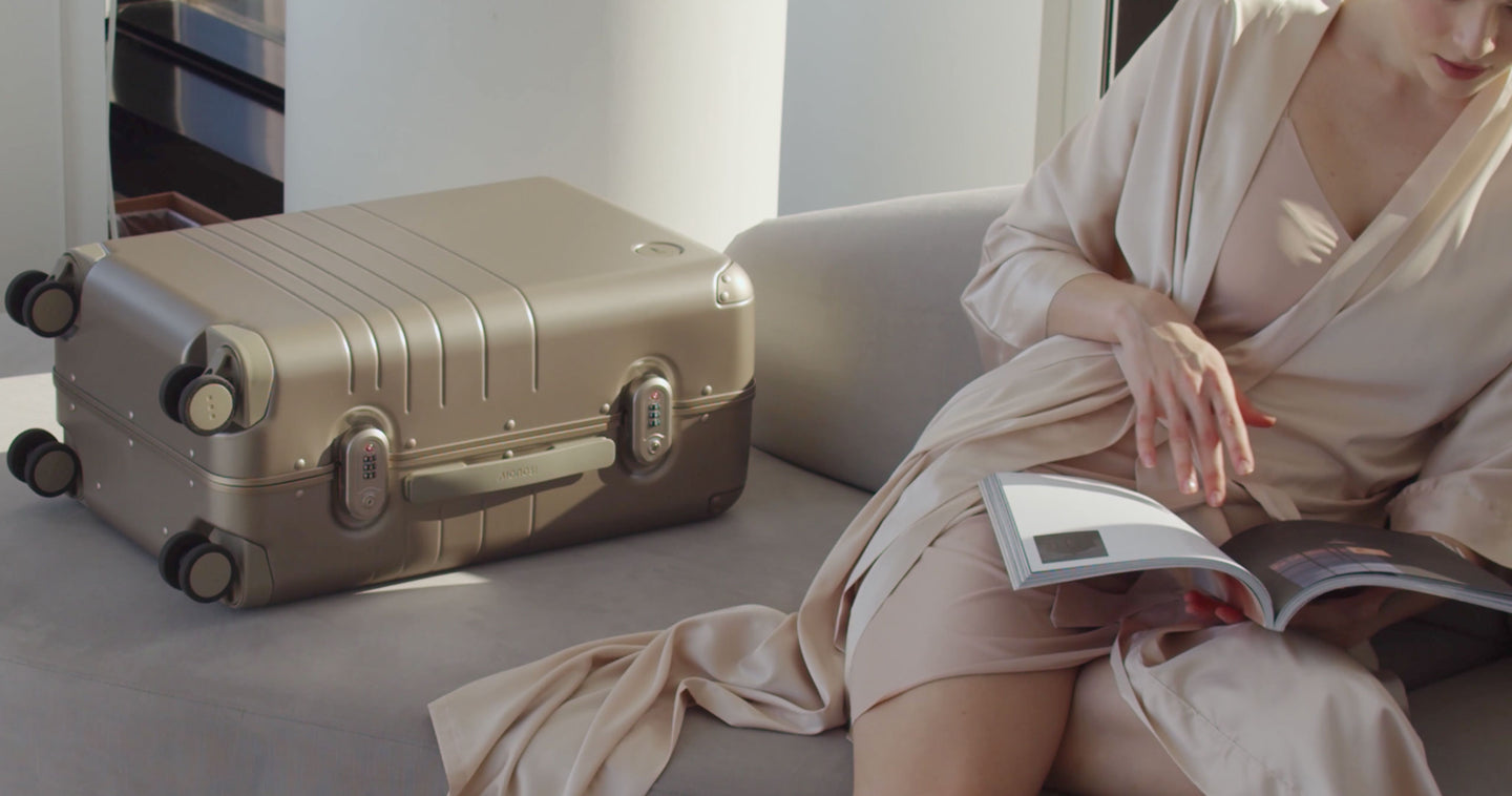 A woman sitting on a couch reading a magazine while a Hybrid Carry-On lays besides her