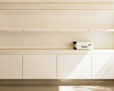 A close-up of a display shelf featuring a single piece of carry-on in desert taupe on a clean, white surface, with warm lighting accenting the minimalist design.