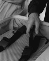 Close-up of hands adjusting the interior compression straps of a Monos carry-on as part of a quality control process.