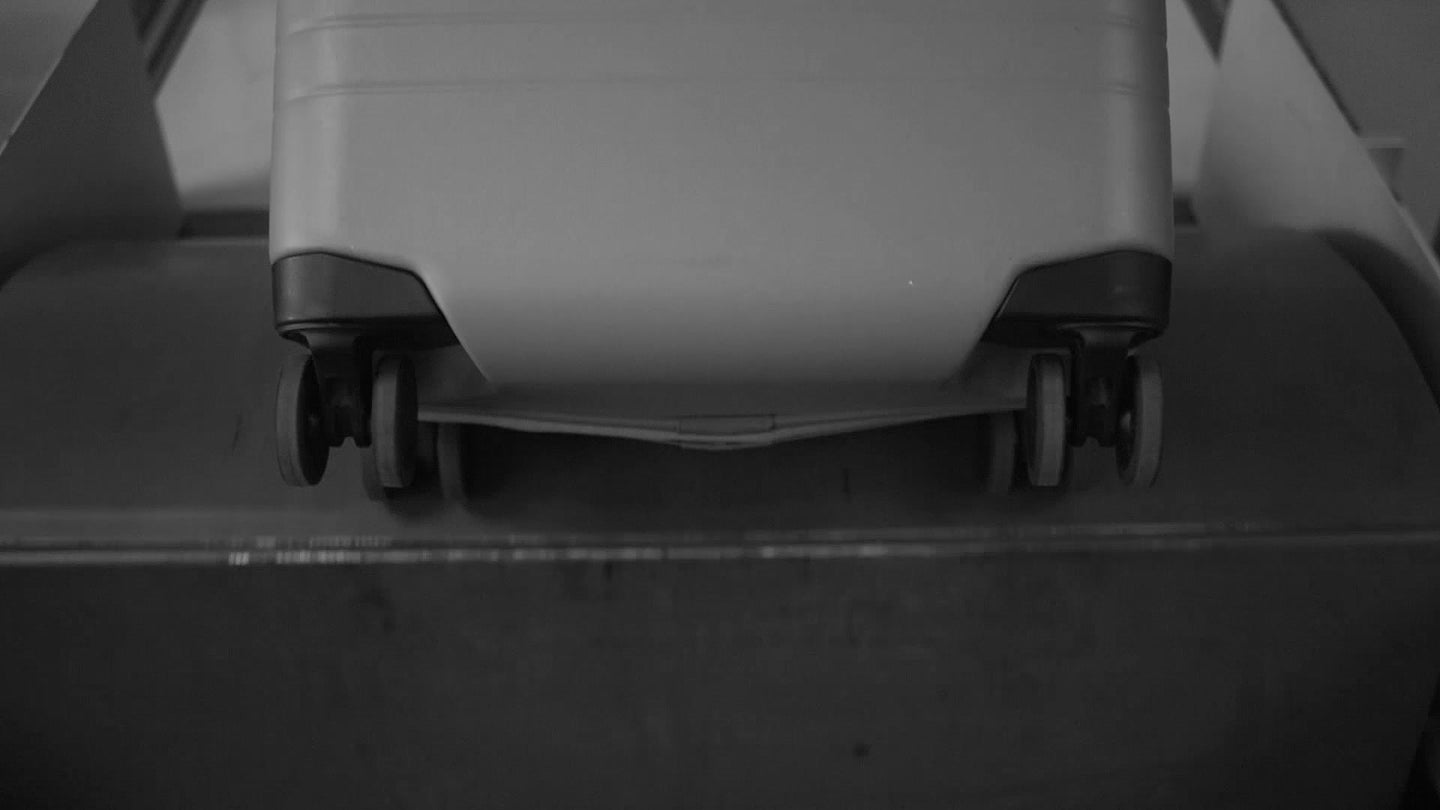Close-up of the base of a Monos Carry-On with wheels being tested on a conveyor-like system, demonstrating the durability of its wheels.