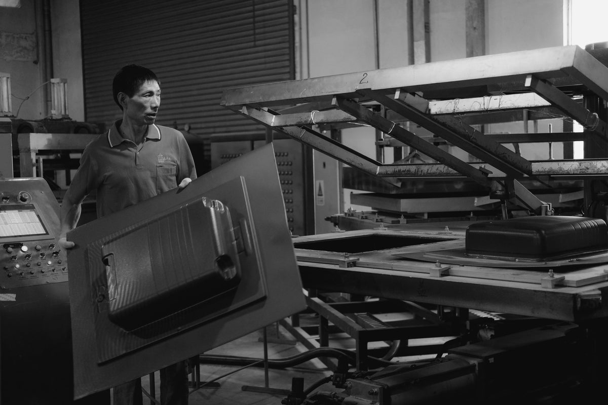 An operator removes a freshly molded Monos luggage shell from a vacuum-forming machine inside the factory.