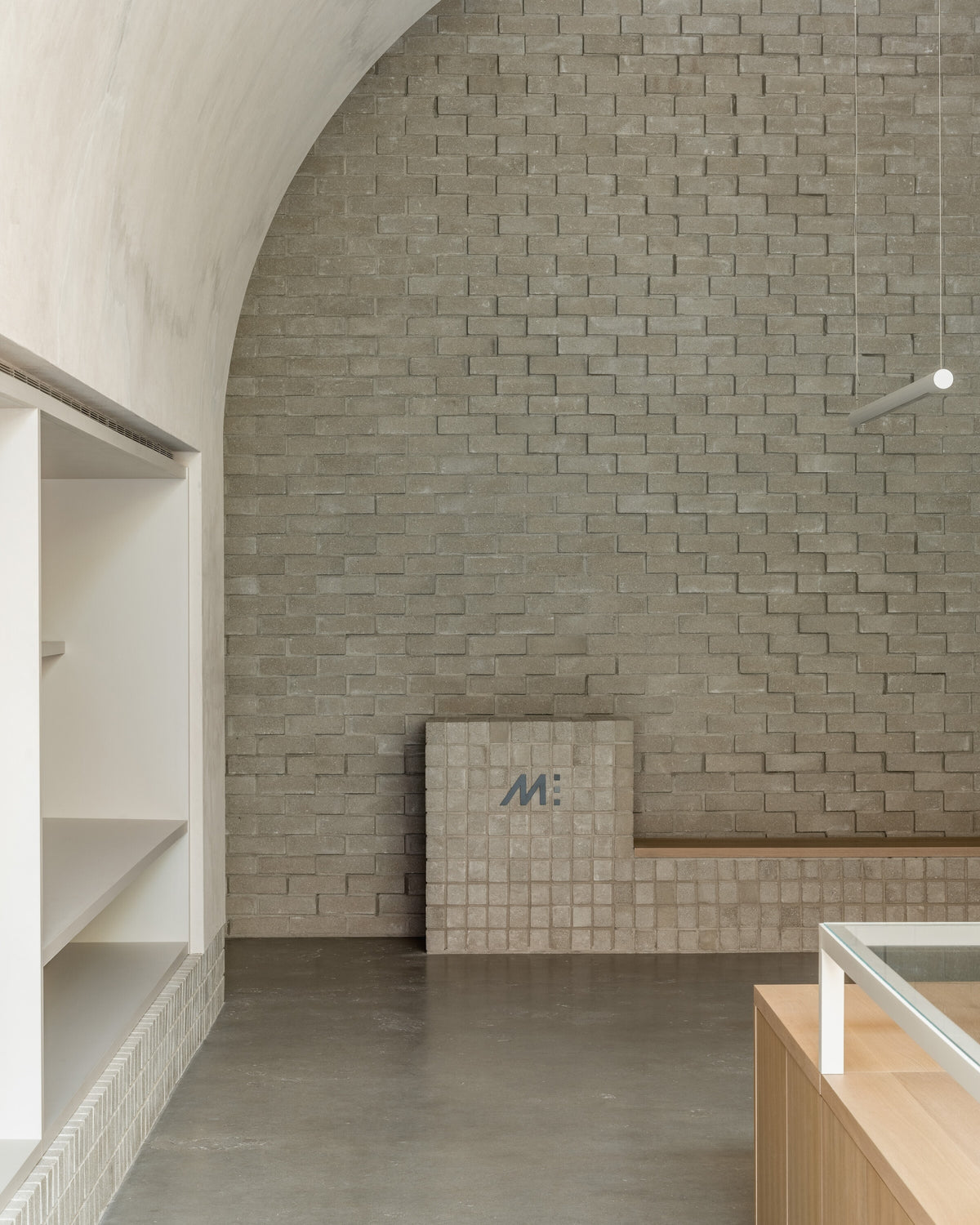 A close-up of a light-gray brick wall with textured, geometric designs. The floor is smooth, and part of a wooden display counter can be seen in the foreground.