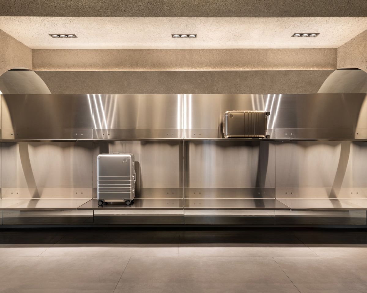 Display wall inside the Monos Georgetown store featuring aluminum luggage showcased against brushed steel shelving and soft ambient lighting.