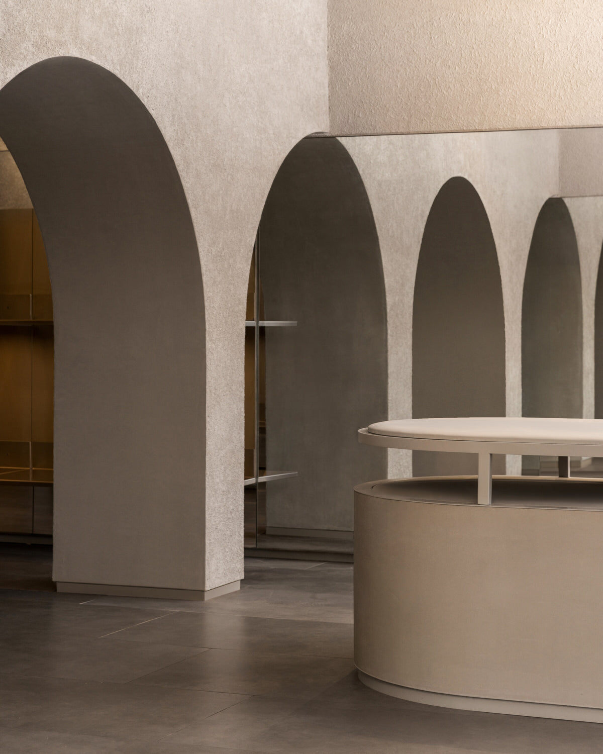 Curved display counter surrounded by soft stone arches inside the Monos Georgetown store, highlighting the minimalist design and warm neutral palette.