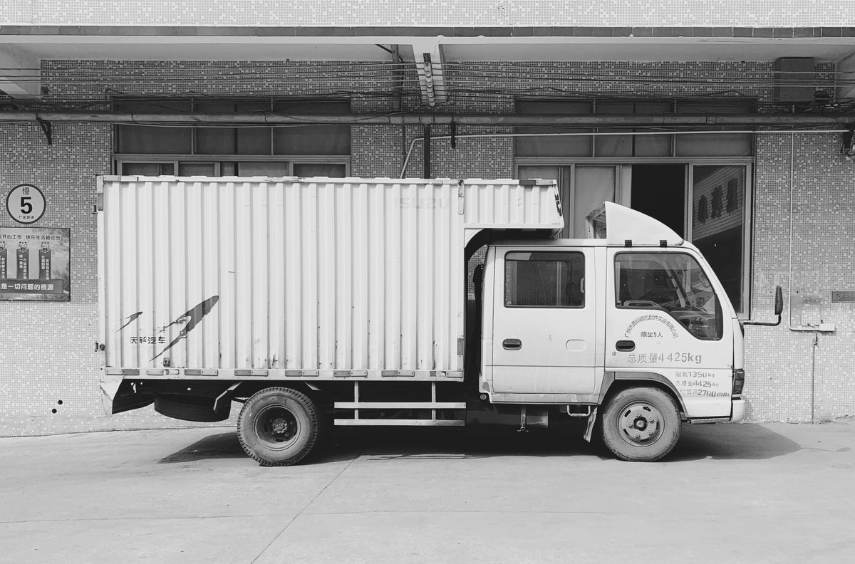 A side view of a truck parked outside a factory, ready for logistics and transportation.
