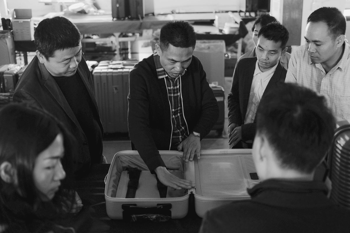 A group of people examining and discussing the interior design of an open Monos Carry-On.