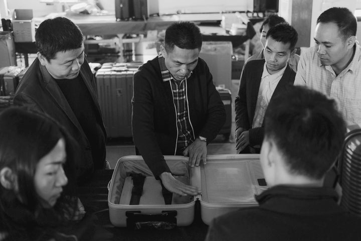 A group of people examining and discussing the interior design of an open Monos Carry-On.