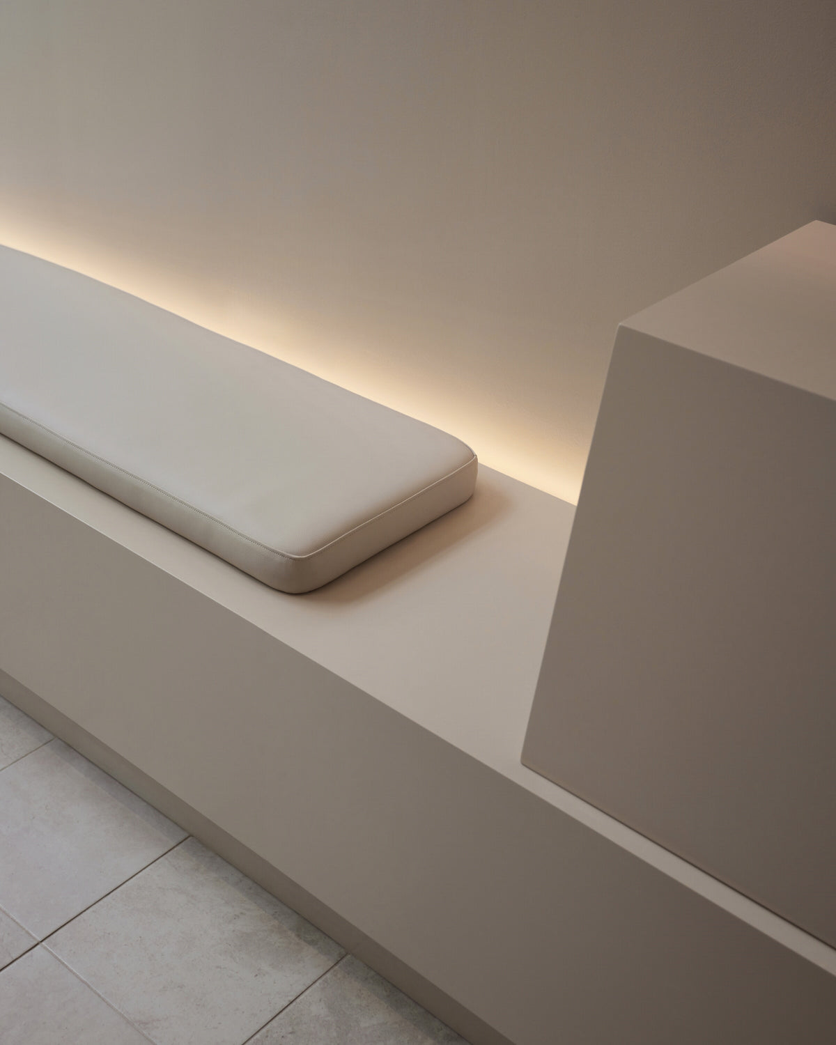 Detail of minimalist seating with a cushioned bench and soft backlighting inside the Monos Boston store.