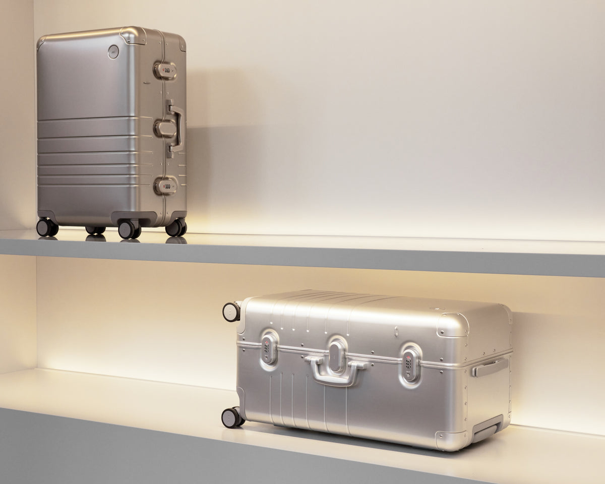 Two silver suitcases on a shelf with a neutral background